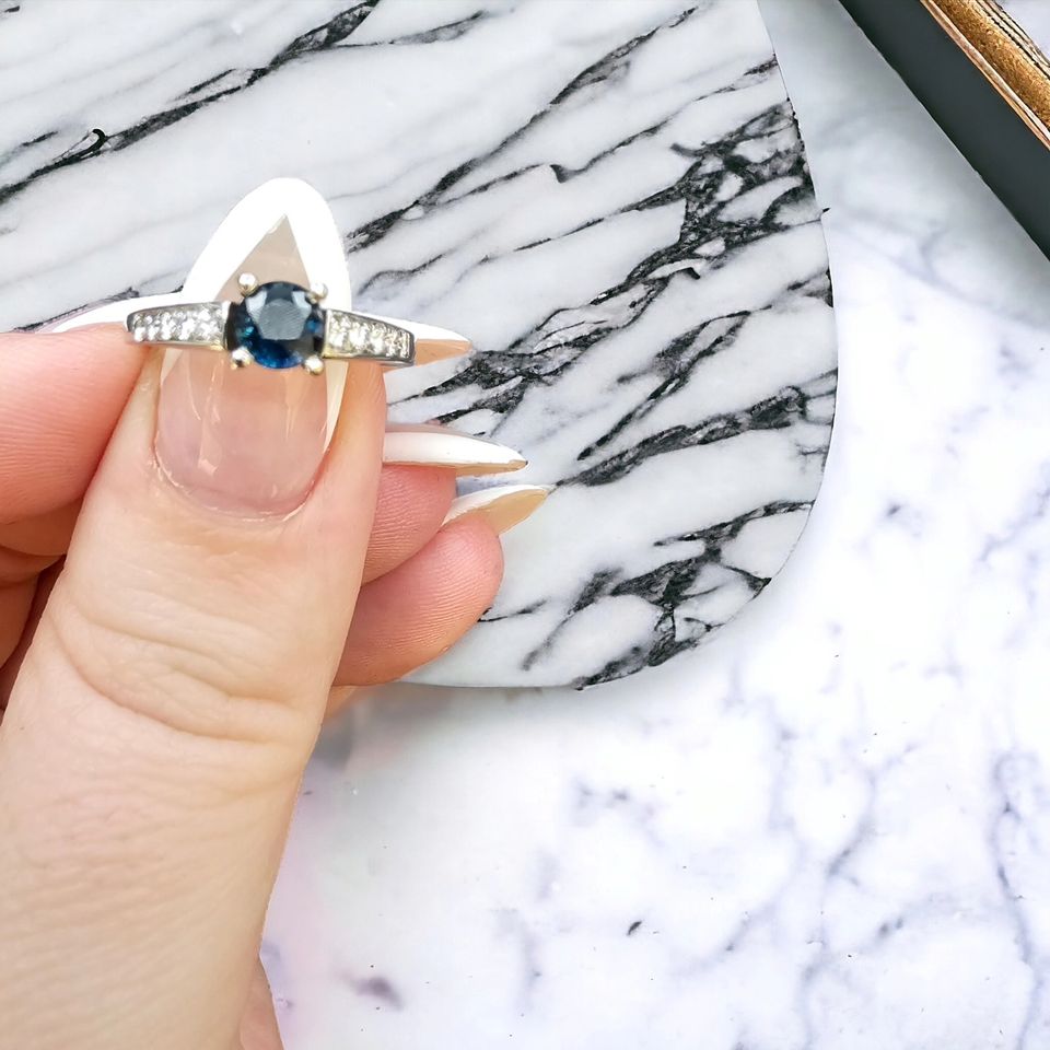 14k white gold ring featuring a blue sapphire center stone surrounded by 10 diamonds.