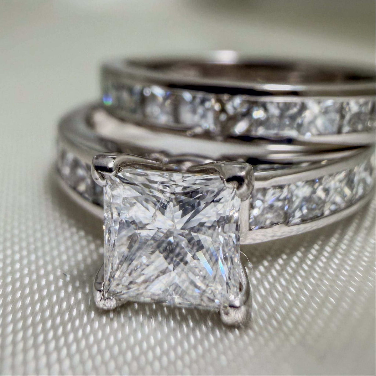 18k White Gold Bridal Rings with a princess-cut diamond solitaire and coordinating bands set with sparkling stones.