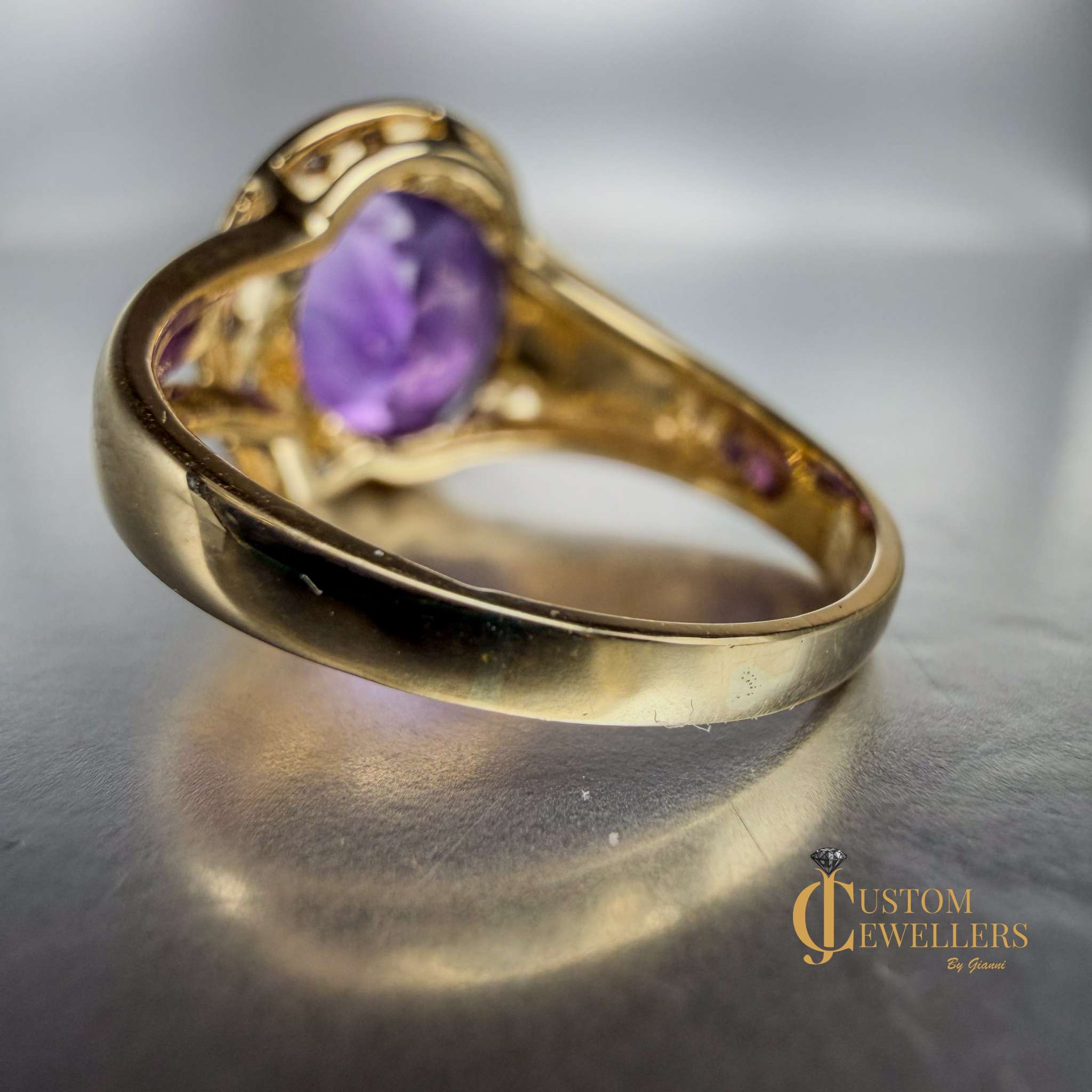 A yellow gold ring featuring a large oval-cut purple amethyst centre stone, accented by small diamonds set along a half-halo edge.