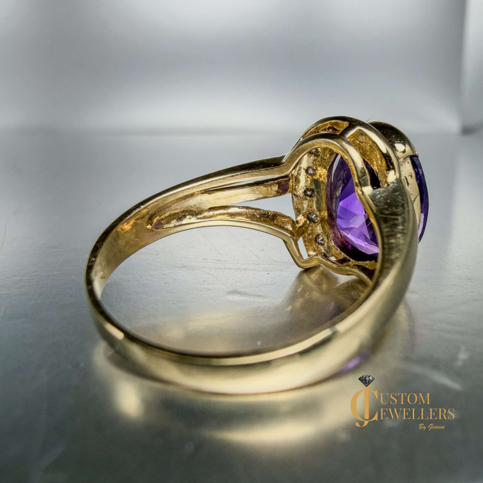 A yellow gold ring featuring a large oval-cut purple amethyst centre stone, accented by small diamonds set along a half-halo edge.