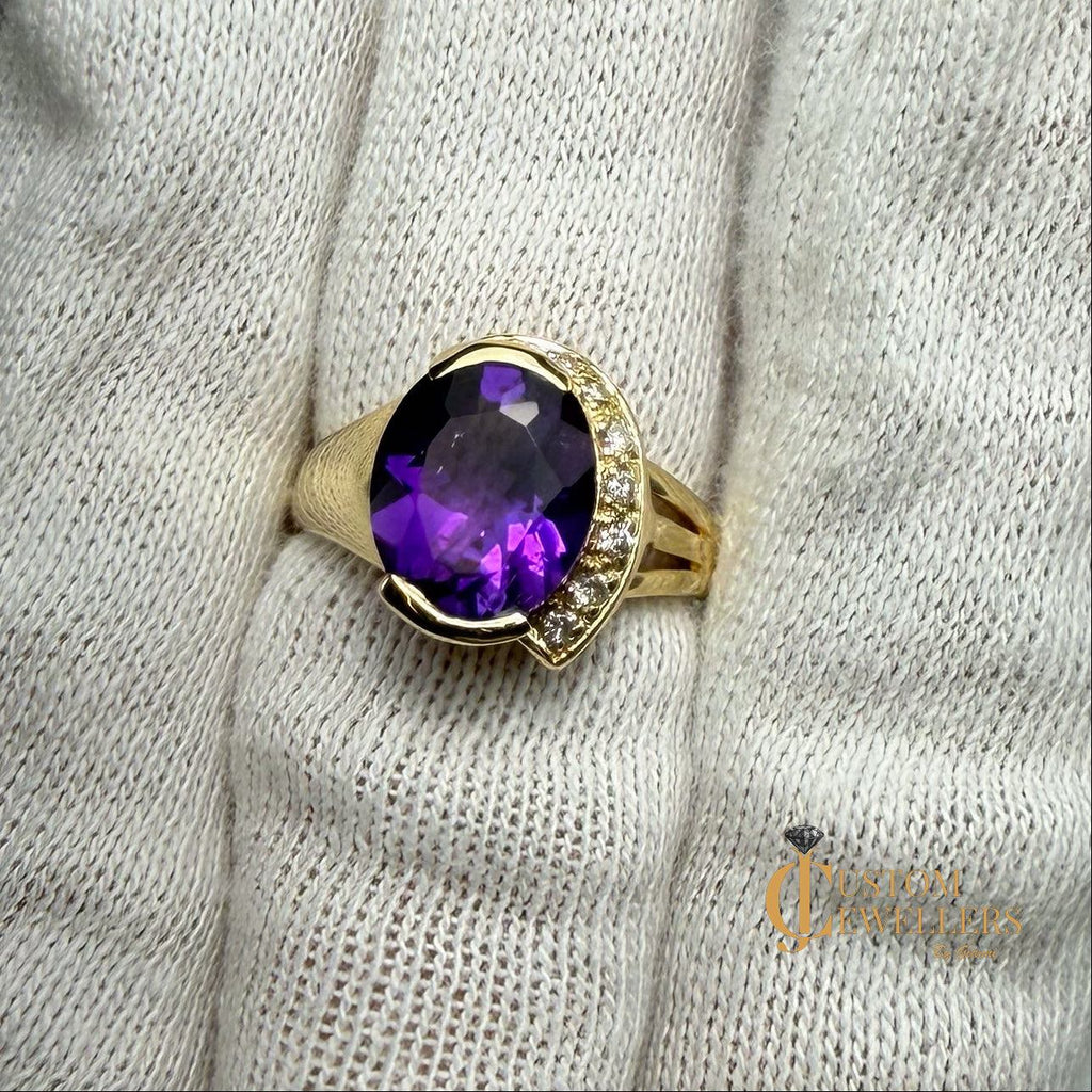 A yellow gold ring featuring a large oval-cut purple amethyst centre stone, accented by small diamonds set along a half-halo edge.