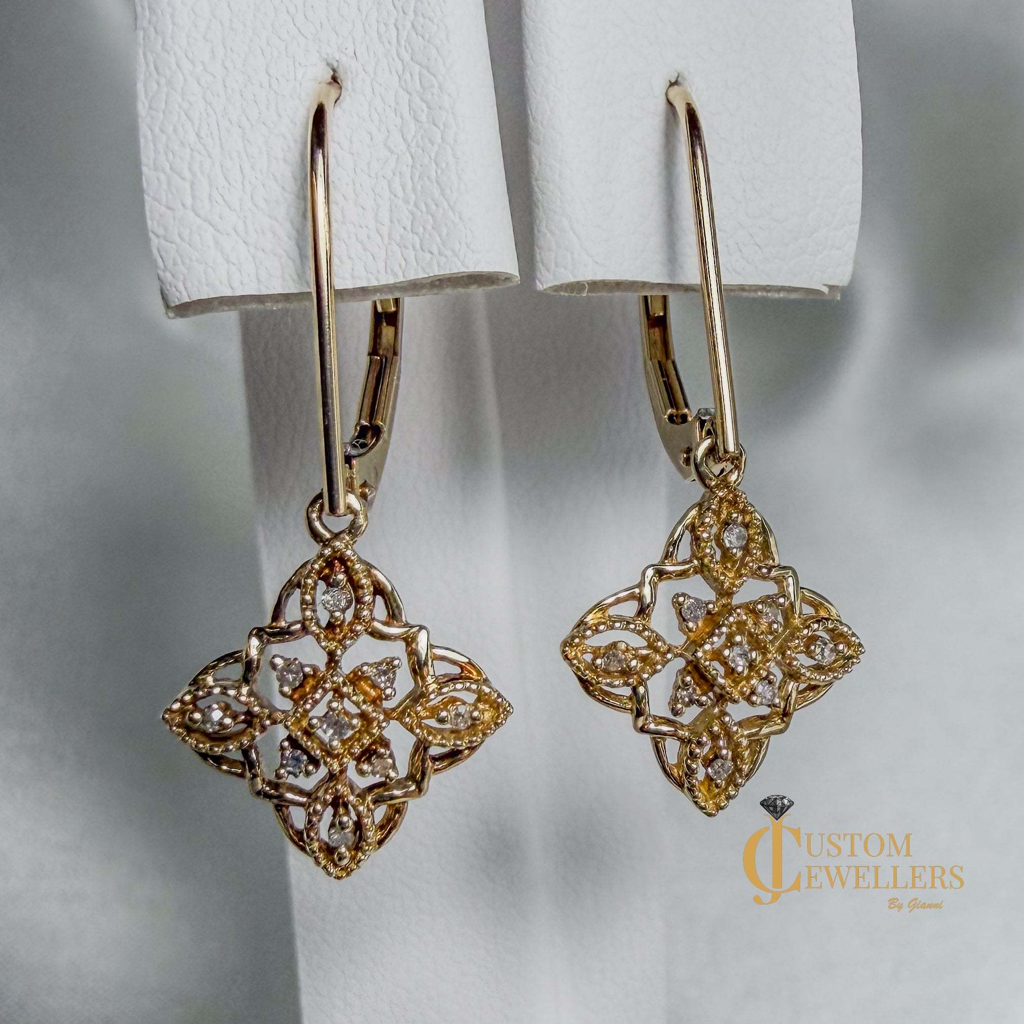 Gold filigree dangle earrings with diamonds, shown hanging against a soft white background. 