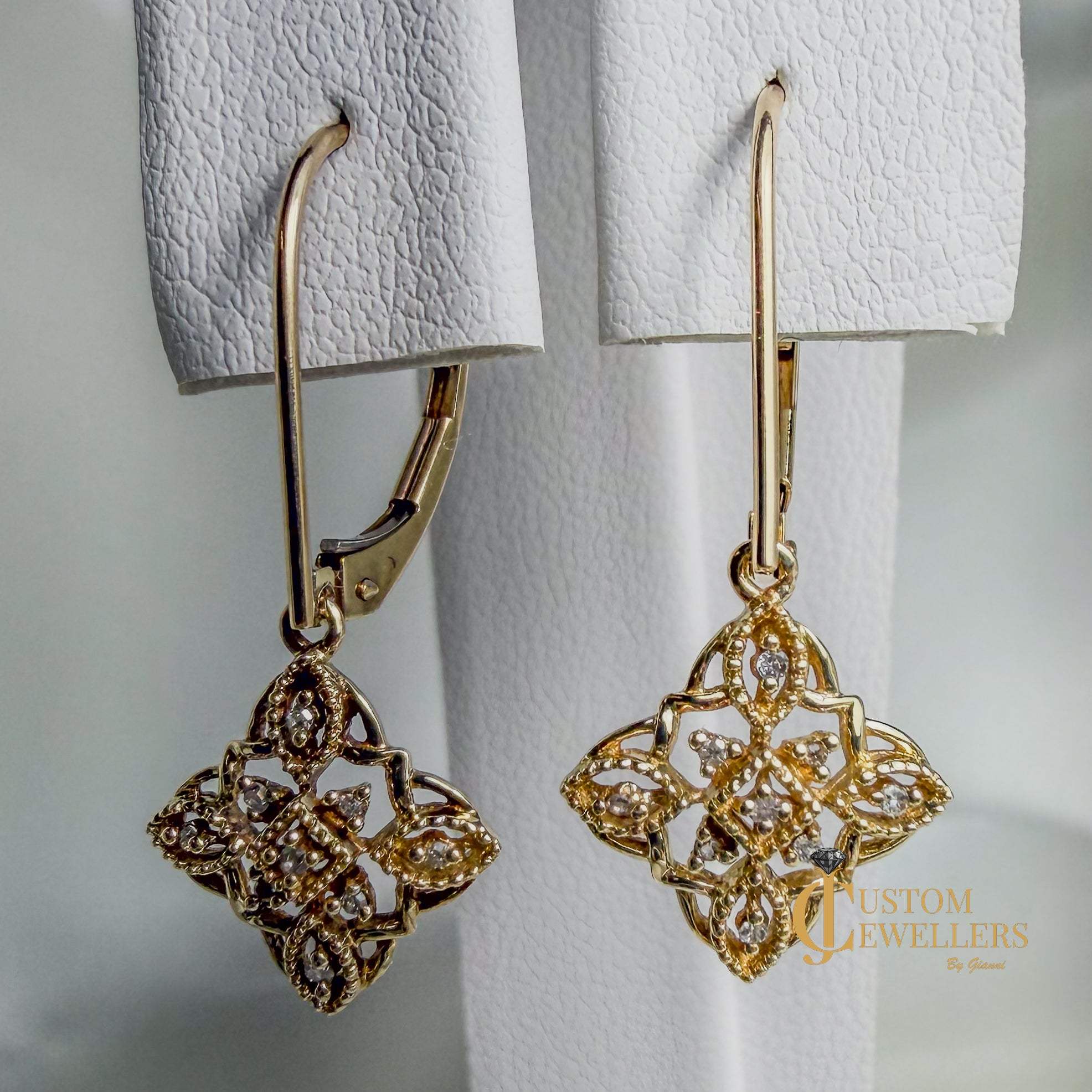 Gold filigree dangle earrings with diamonds, shown hanging against a soft white background. 