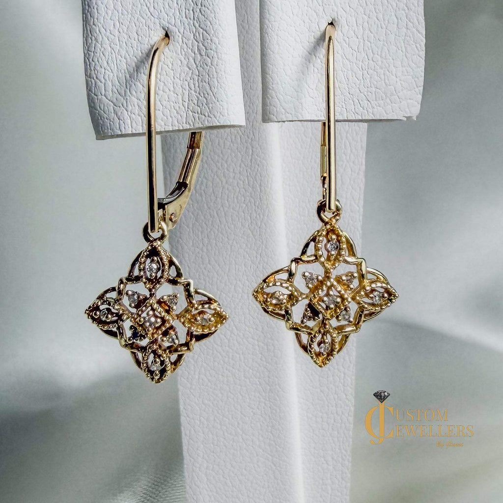 Gold filigree dangle earrings with diamonds, shown hanging against a soft white background. 