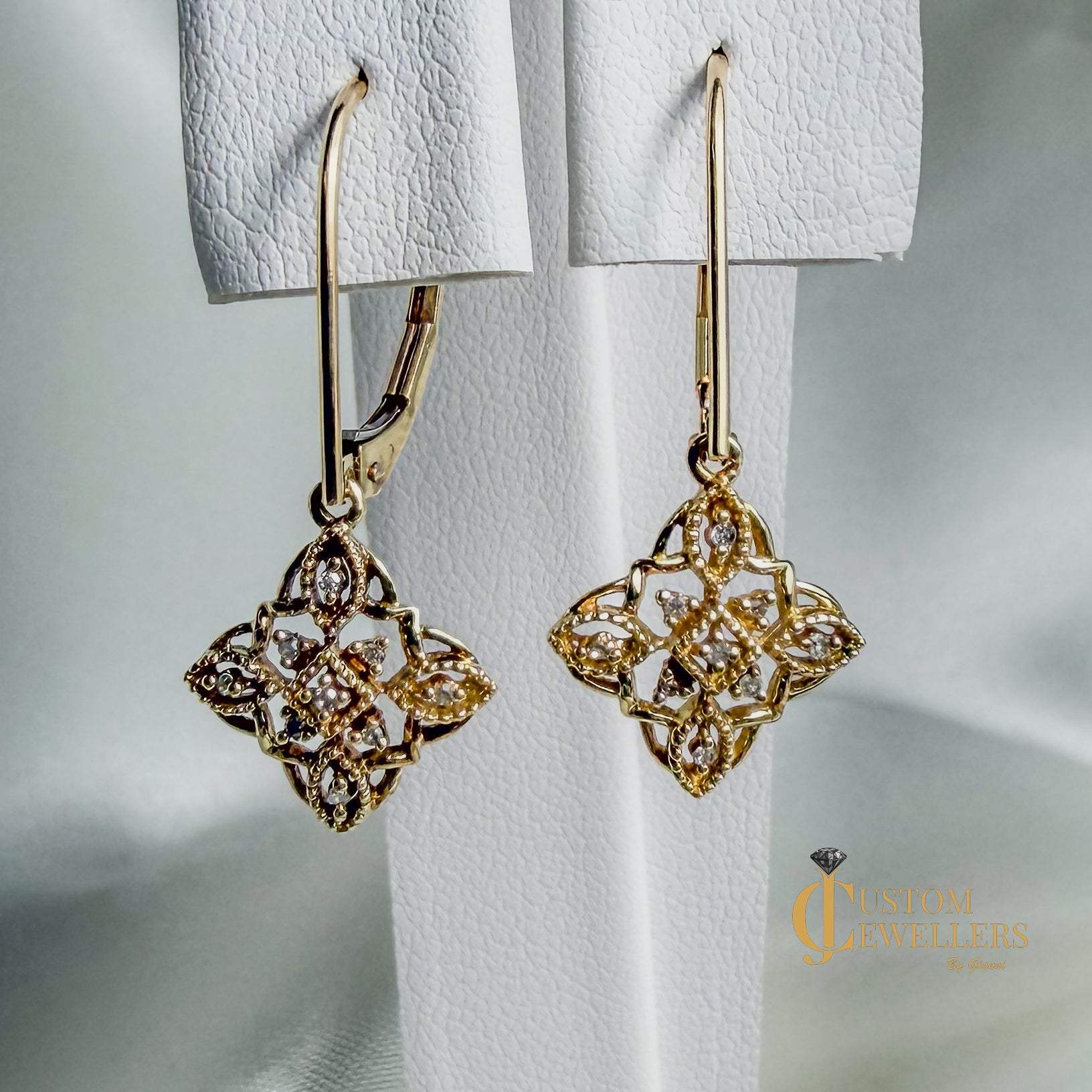 Gold filigree dangle earrings with diamonds, shown hanging against a soft white background. 