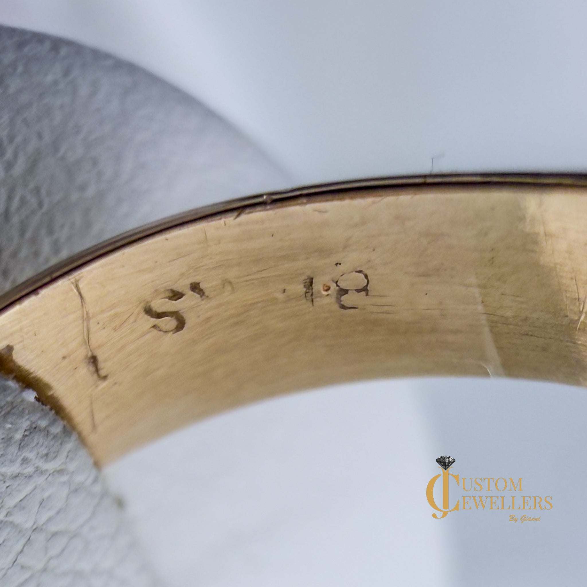 Gold ring with engraved text on a white background, featuring 'Custom Jewellers'.