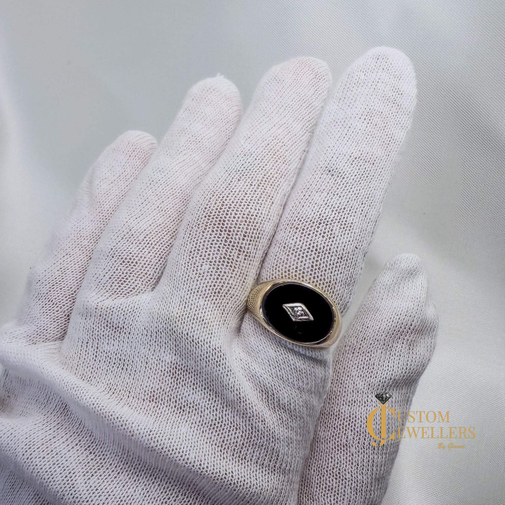 Hand wearing a white glove holding a ring with a black stone and gold band on a light gray background.