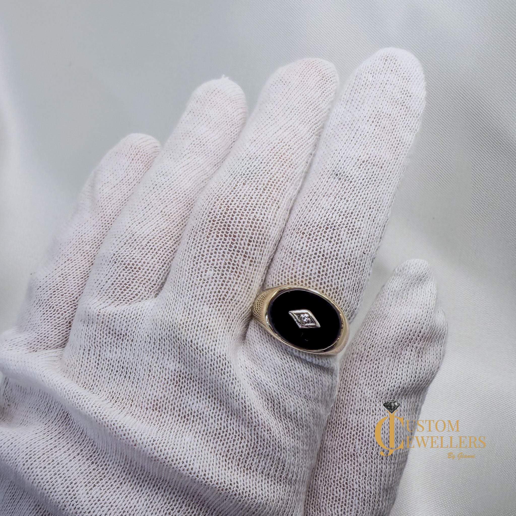 Hand wearing a white glove holding a ring with a black stone and gold band on a light gray background.