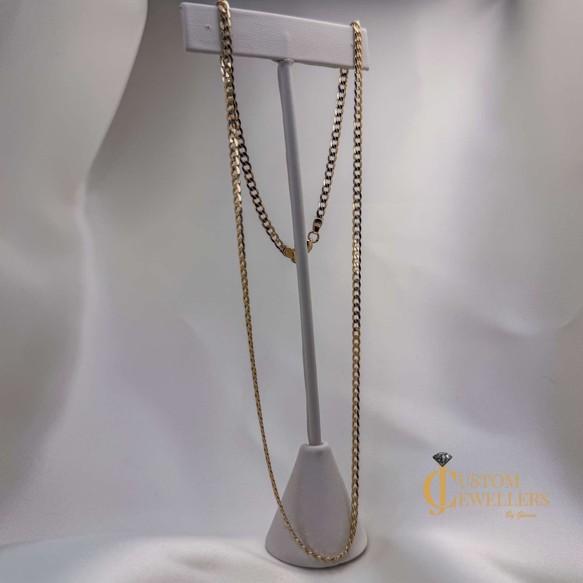 Gold chain necklace on a white stand with a gray background