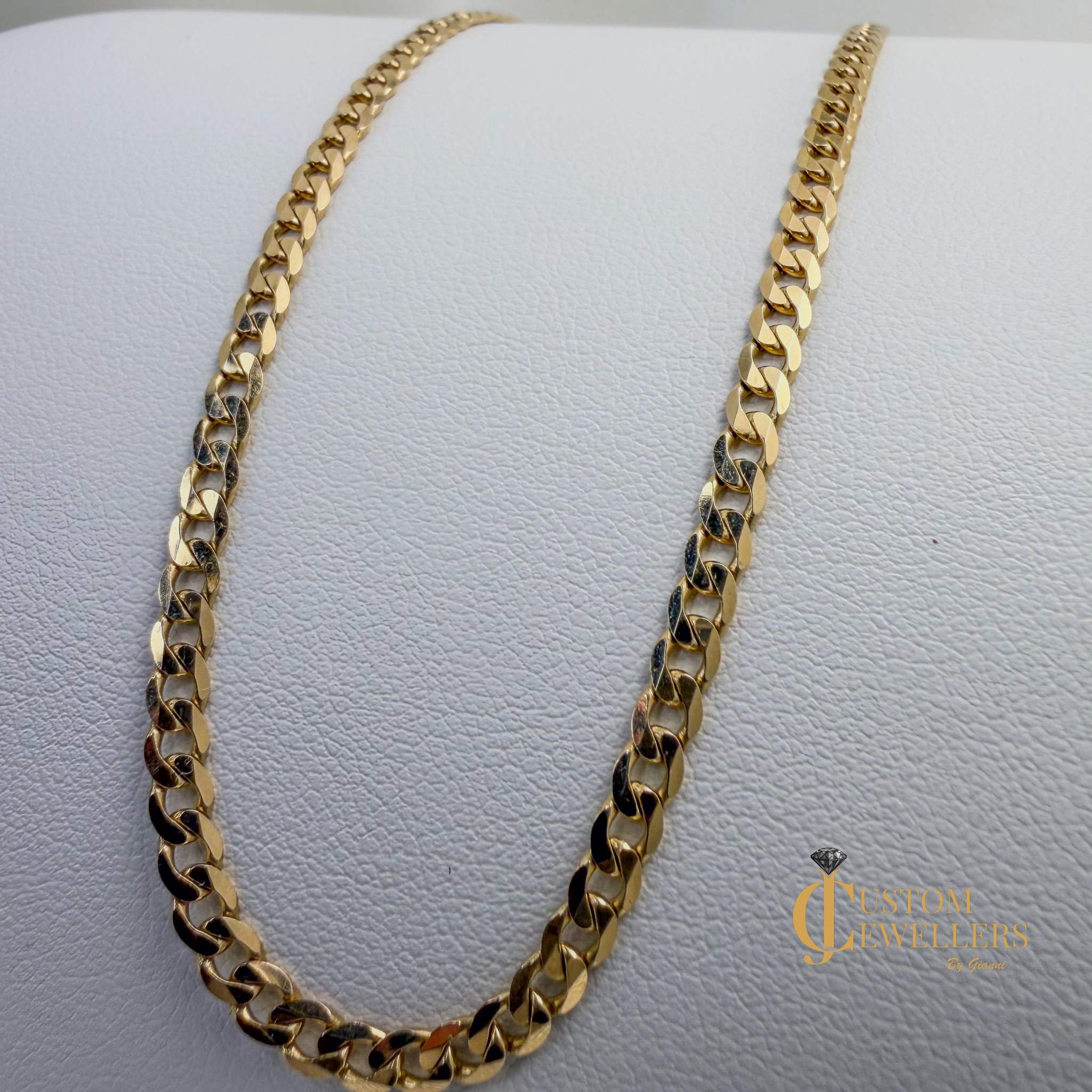 Gold chain necklace on a textured gray surface with 'Custom Jewelers' branding.