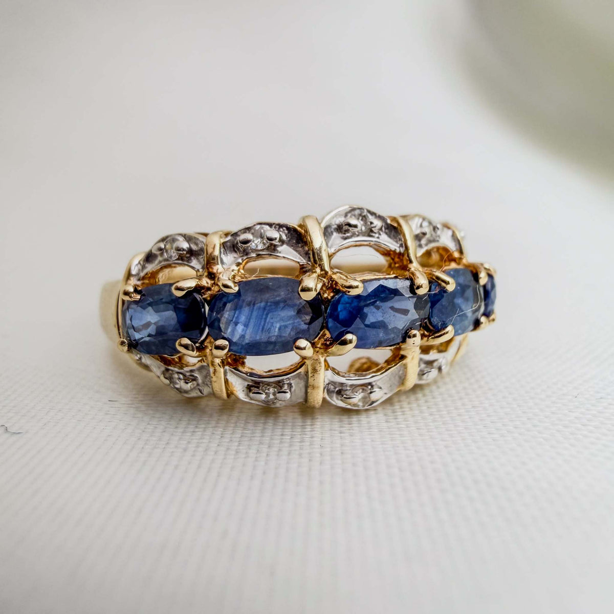 Blue Sapphire and VS Diamond ring with deep blue oval stones, yellow gold prongs, and sculpted silver-tone accents set with small clear stones.